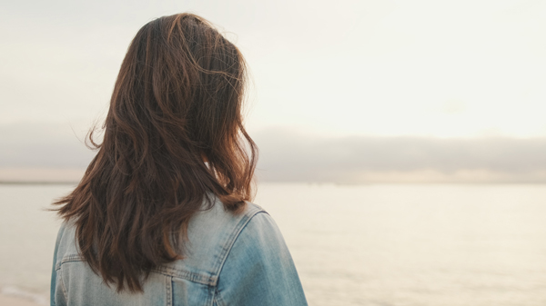 woman with long hair wearing denim jacket looking at calm ocean during sunset serene moment in nature